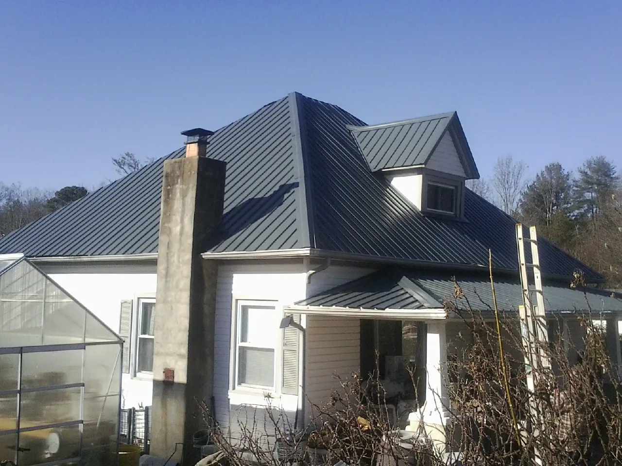 Dark blue standing seam metal roof on a white farmhouse with dormer — Slate & Tile Roof Repair by Roofing Brothers in Hurst