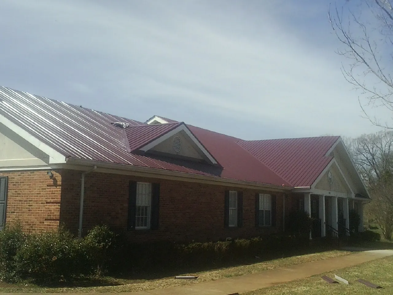Red metal roof with gabled entries on a long brick building, from a Hail Damage Roof Repair job in Hurst