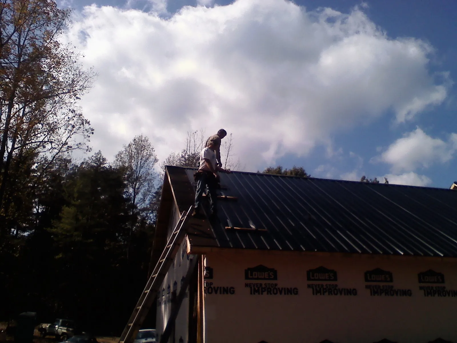 Roofer fastening dark metal panels high against a cloudy sky, from a Roof Inspection job in Hurst