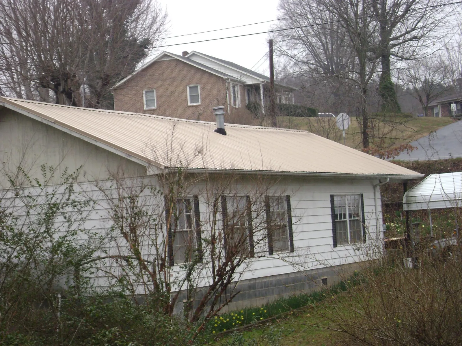 Tan metal roof on a white sided house set into a hillside — Commercial Roofing by Roofing Brothers in Hurst