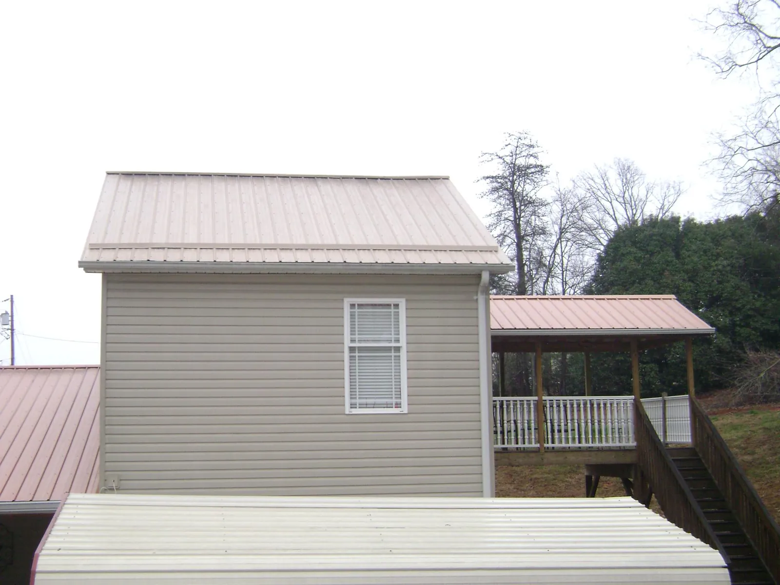 Tan metal roofs on a two story addition and attached porch, from a Roof Replacement job in Hurst